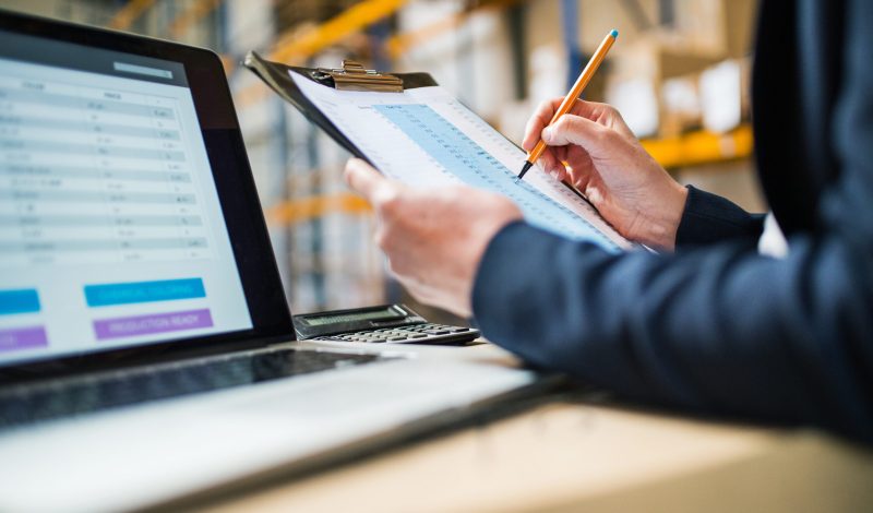 Unrecognizable senior warehouse woman manager or supervisor with a laptop controlling stock.