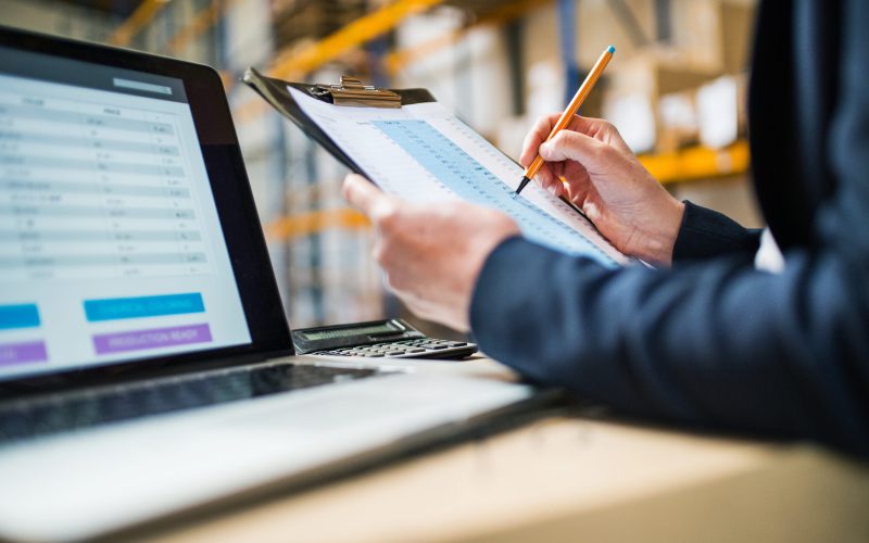 Unrecognizable senior warehouse woman manager or supervisor with a laptop controlling stock.